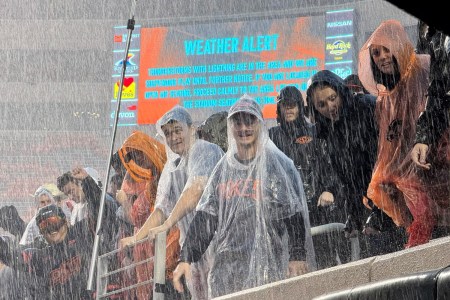 College football fans in the rain. A recent NCAA agreement allowing schools to directly pay student athletes may increase prices for fans.