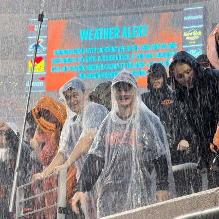 College football fans in the rain. A recent NCAA agreement allowing schools to directly pay student athletes may increase prices for fans.