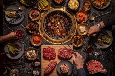 Steak being cooked over an open flame with spices and sides, Korean barbecue-style