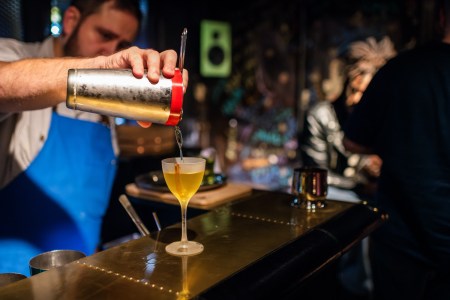 Bartender pouring a drink from a shaker into a coupe