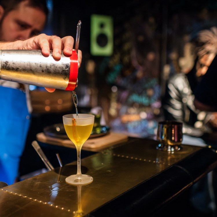 Bartender pouring a drink from a shaker into a coupe