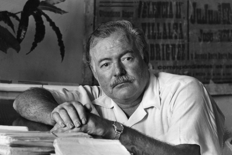 American writer Ernest Hemingway leaning on the desk of his office