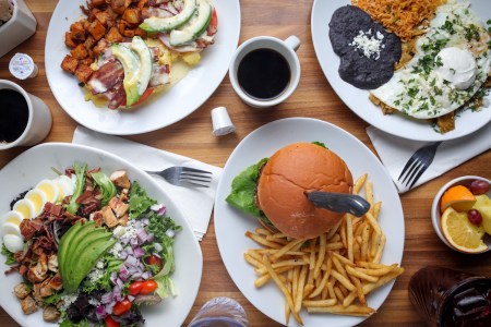 a brunch spread with eggs, potatoes, a cobb salad, burger, fruit salad and coffees