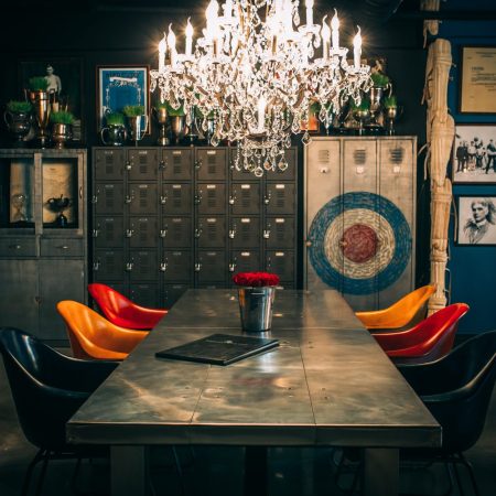 Table with multi-colored seats in front of rustic looking furniture, archery board and a large chandelier