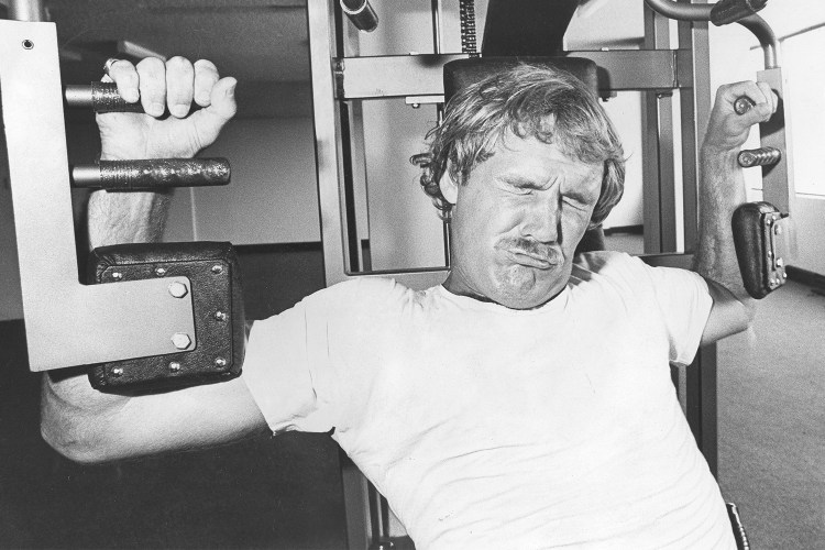 A tired man struggles to push a weighted machine at the gym. Black and white photo.