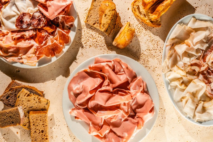 three plates of cured meats and some bread sitting on a tan concrete table