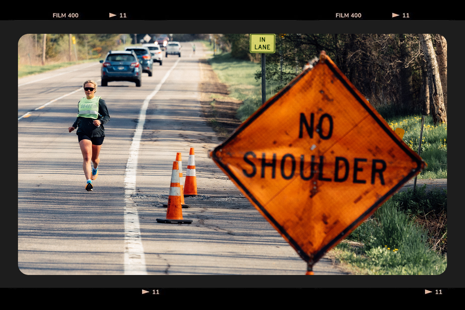 A runner on the side of the road with a sign in the foreground that reads "NO SHOULDER."