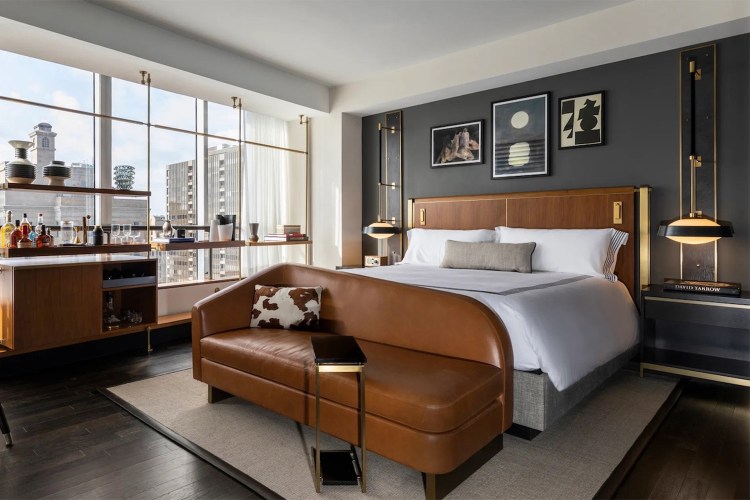 Bedroom in Thompson Dallas with brown leather bedframe, white bedding, floor-to-ceiling window view of city and high quality room accents