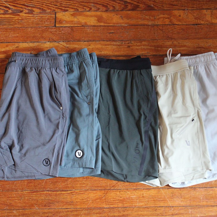 A variety of Vuori shorts spread across a wooden floor. We reviewed five different Vuori shorts for men.